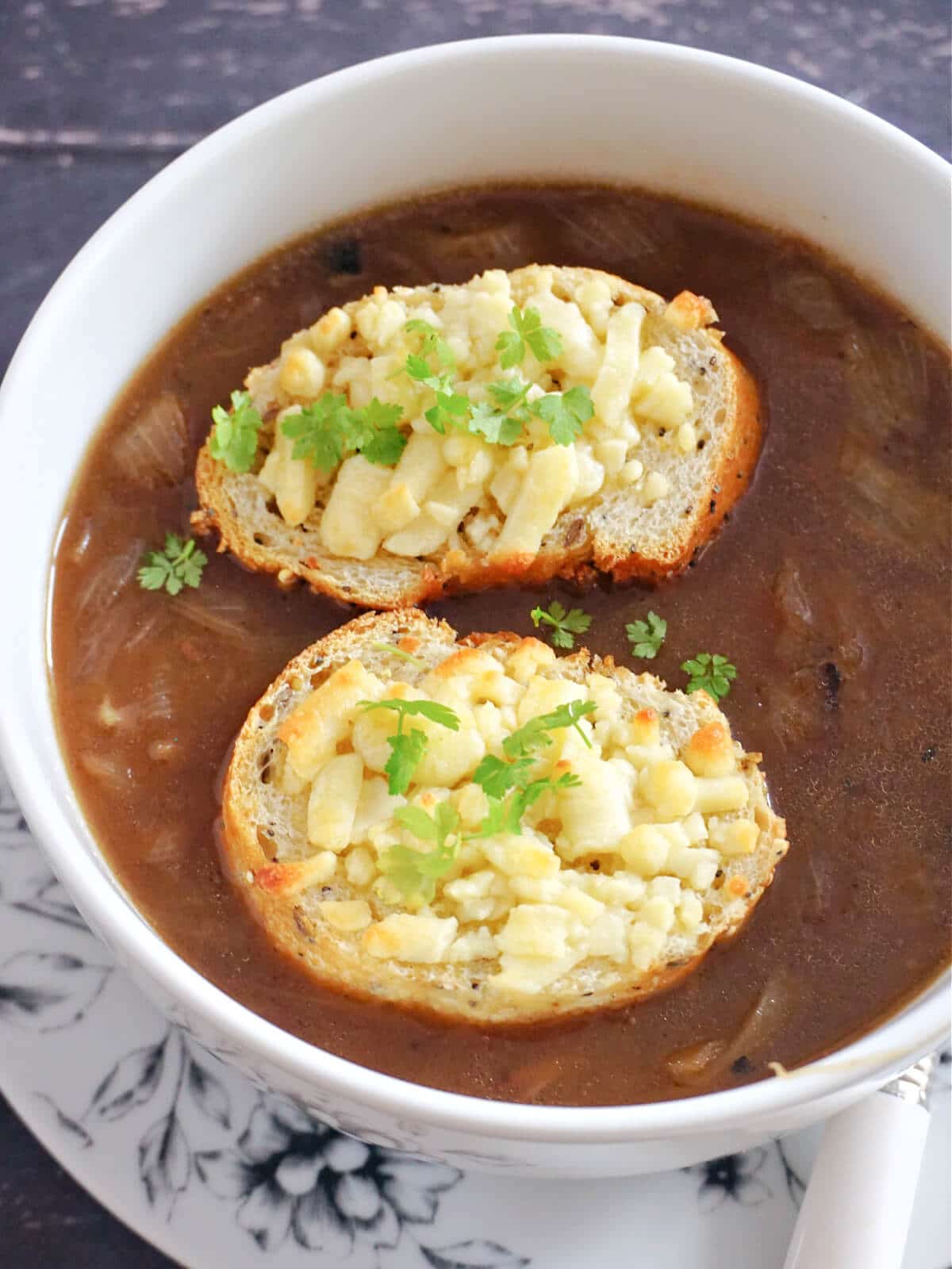 A white bowl of onion soup topped with 2 cheesy slices of baguette and green onions