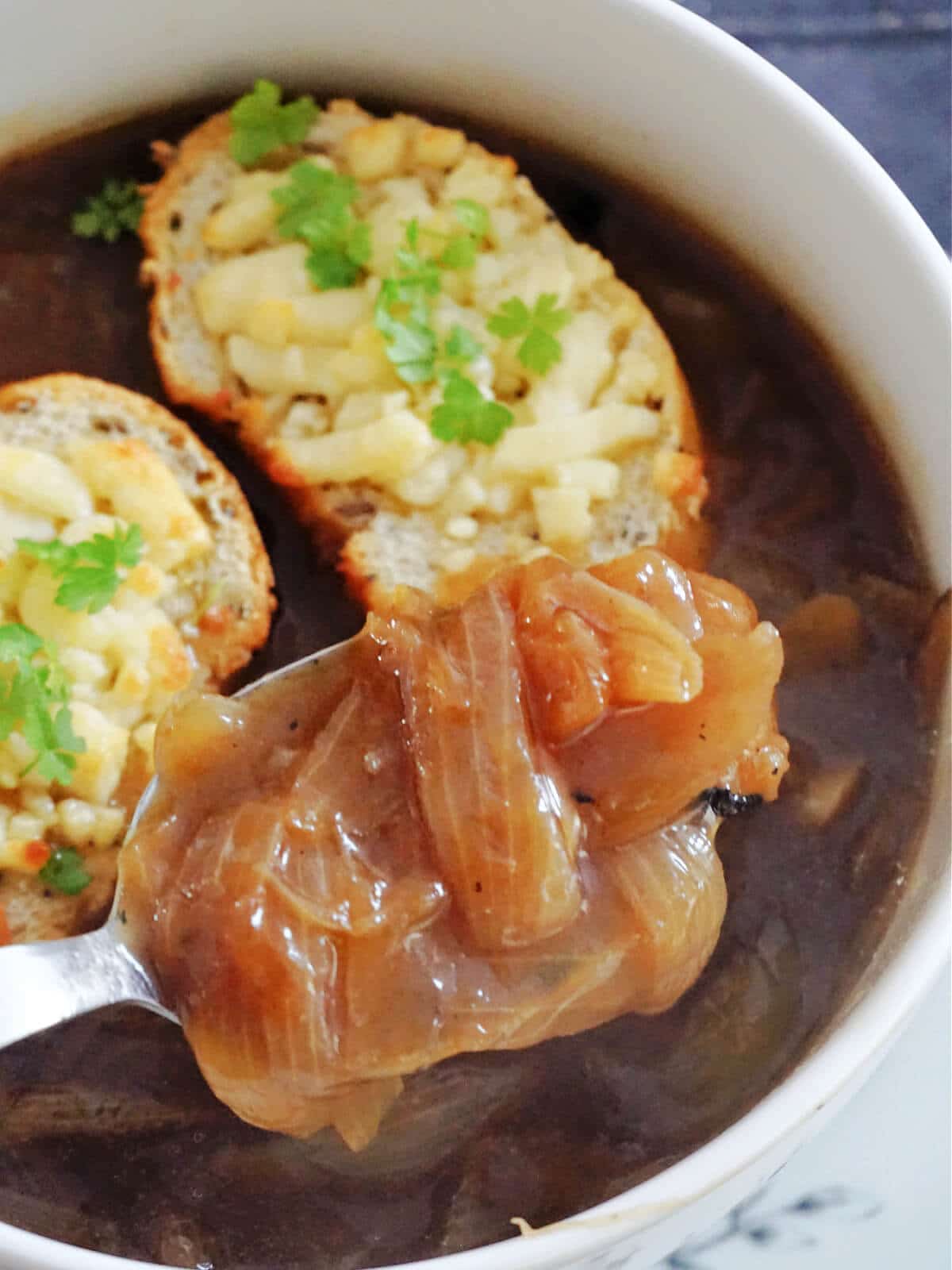 Close-up shot of a white bowl of onion soup with 2 cheesy baguette slices in.