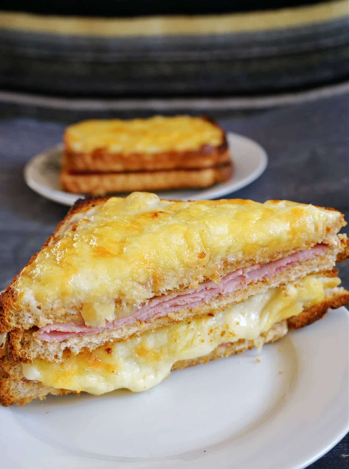 Half of a croque monsieur sandwich on a white plate with another plate with a whole sandwich in the background.