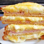 A stack of croque monsieur sandwiches cut in half on a white plate