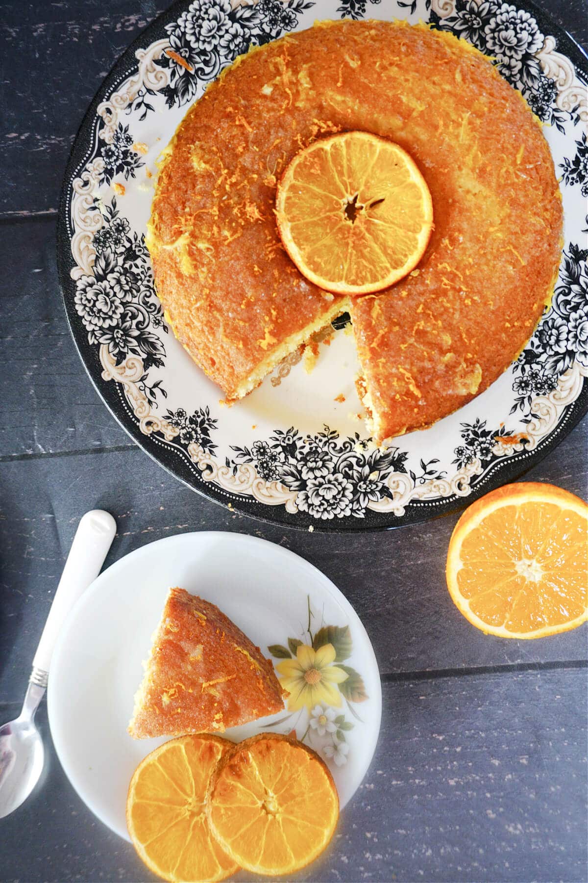 Overhead shot of a white dessert plate with a slice of orange drizzle cake and another larger plate with the rest of the cake topped with an orange slice