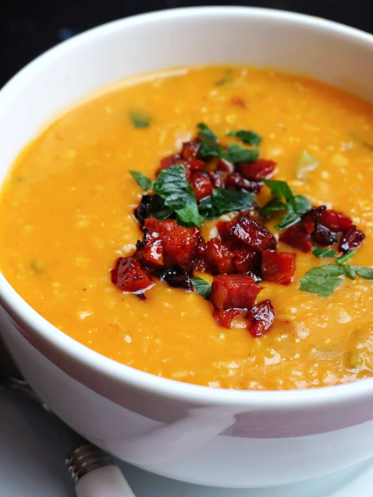Close-up shot of a white bowl with lentil and chorizo soup.