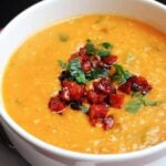 A white bowl of red lentil topped with diced cooked chorizo and parsley