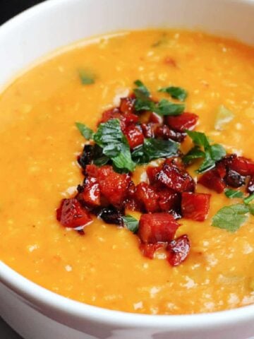 A white bowl of red lentil topped with diced cooked chorizo and parsley