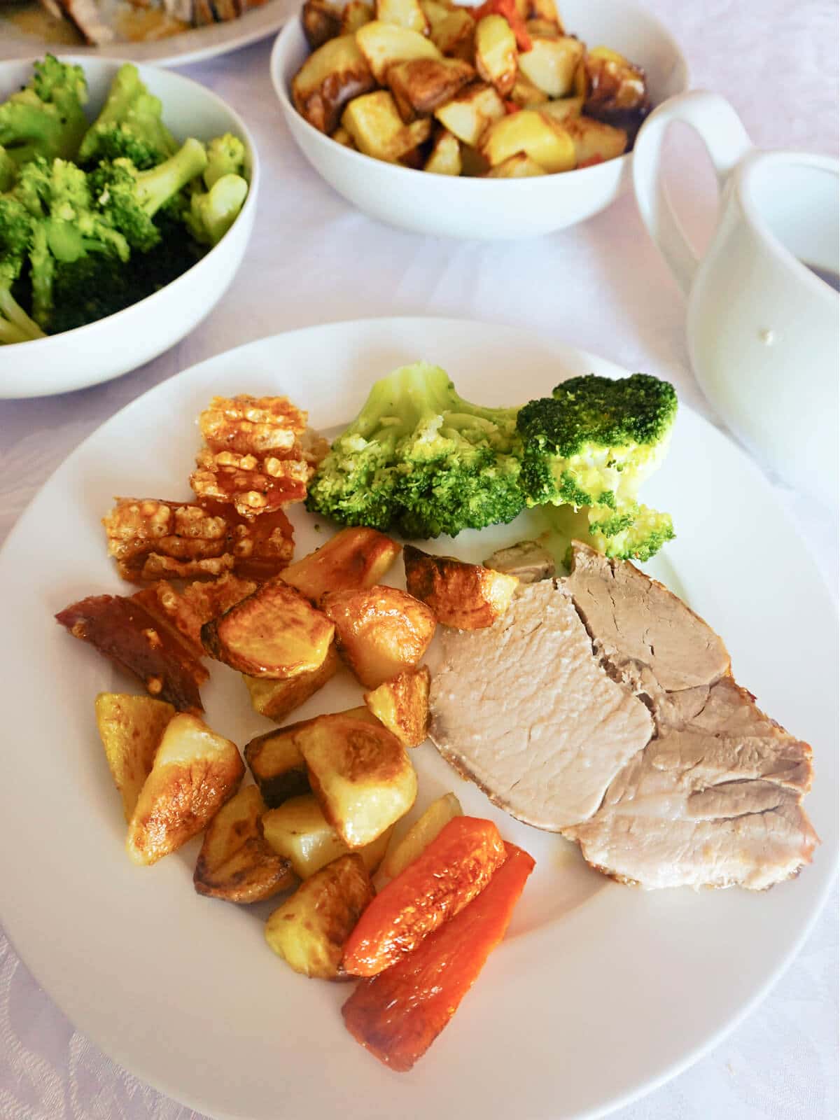A white plate with a slice of roast pork, roasted vegetables and broccoli.