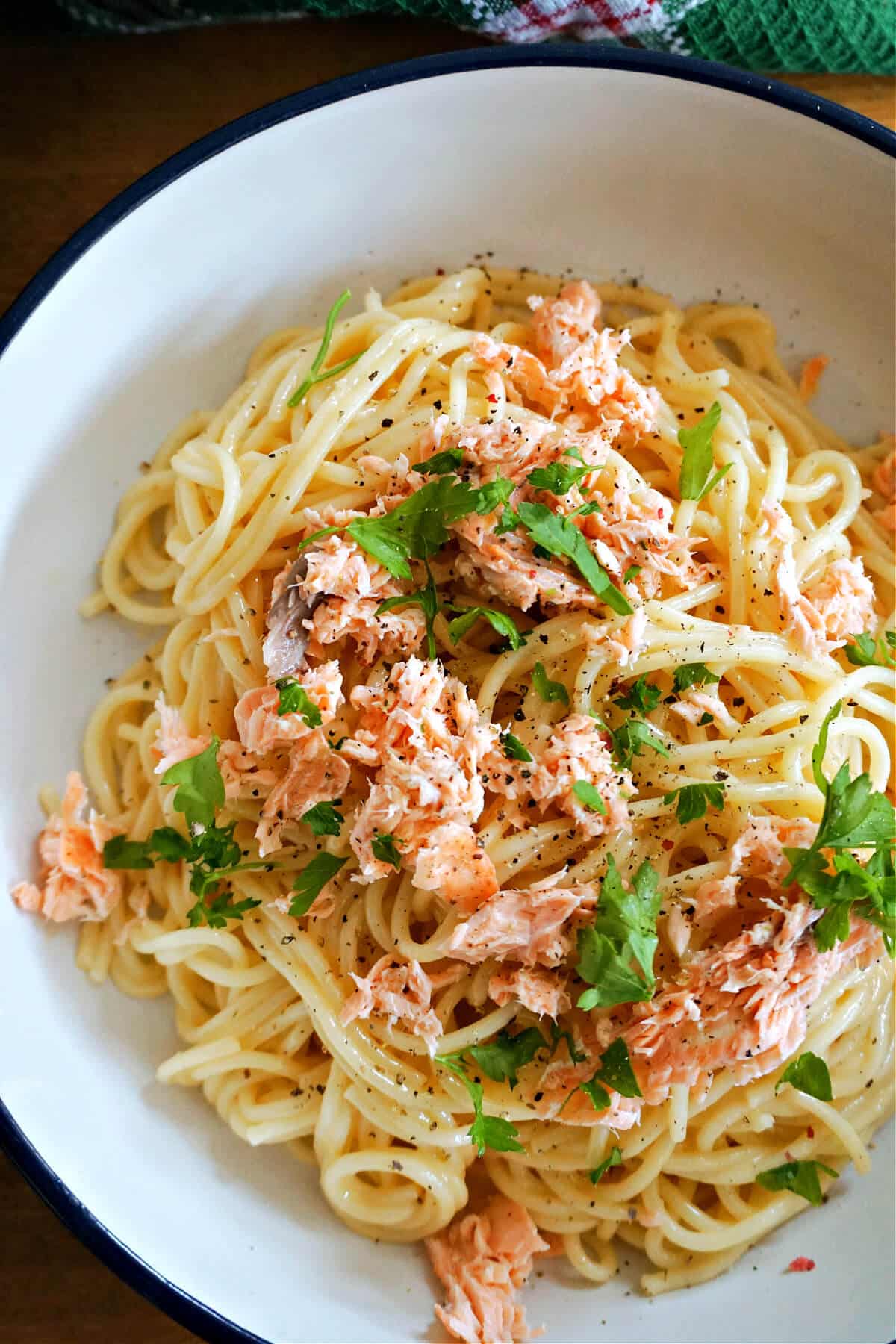 A white bowl with spaghetti carbonara topped with salmon flakes and parsley.