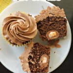 2 halves of a creme egg cupcake and a whole cupcake on a white plate.