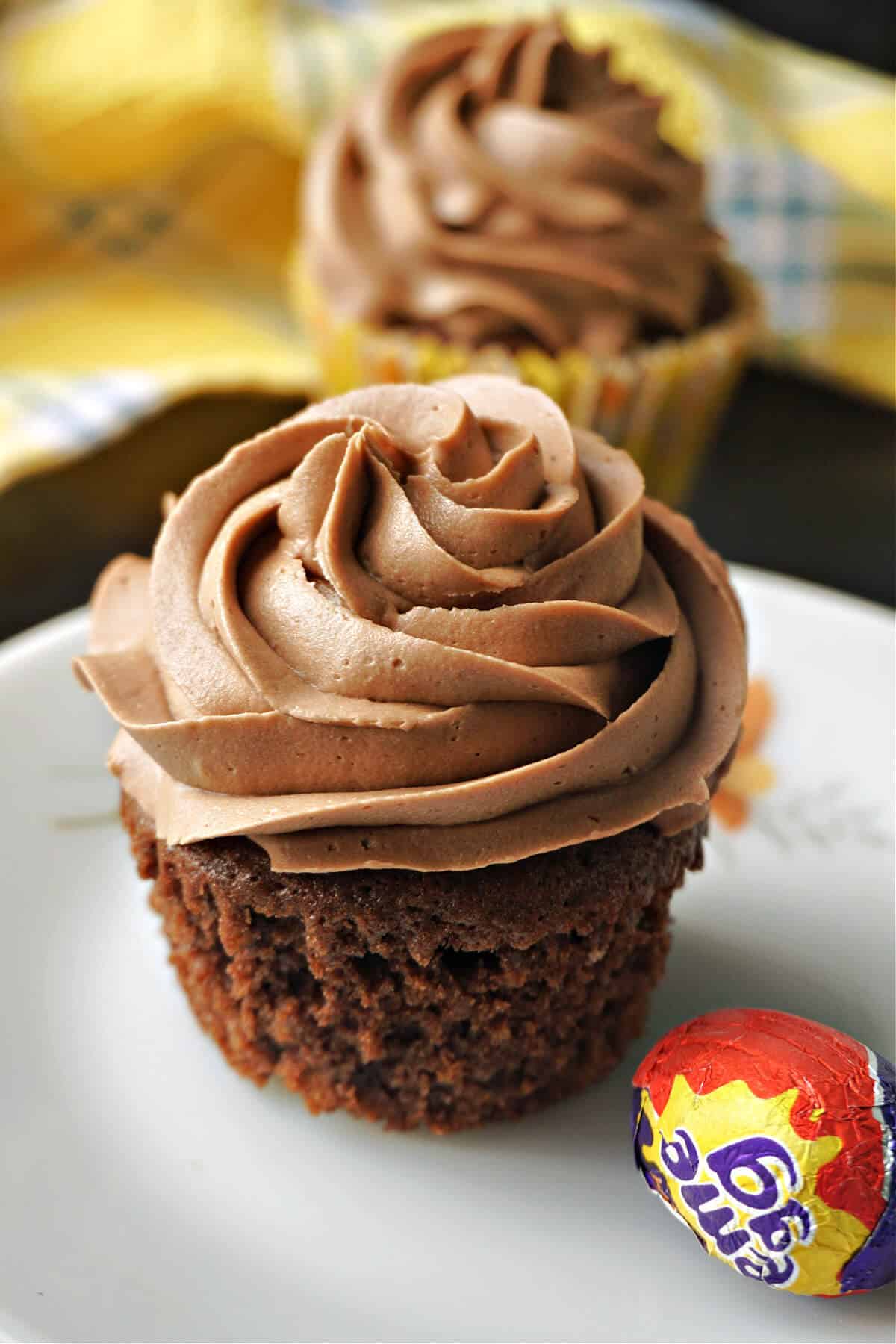 A chocolate cupcake on a white plate with a mini creme egg on the side.