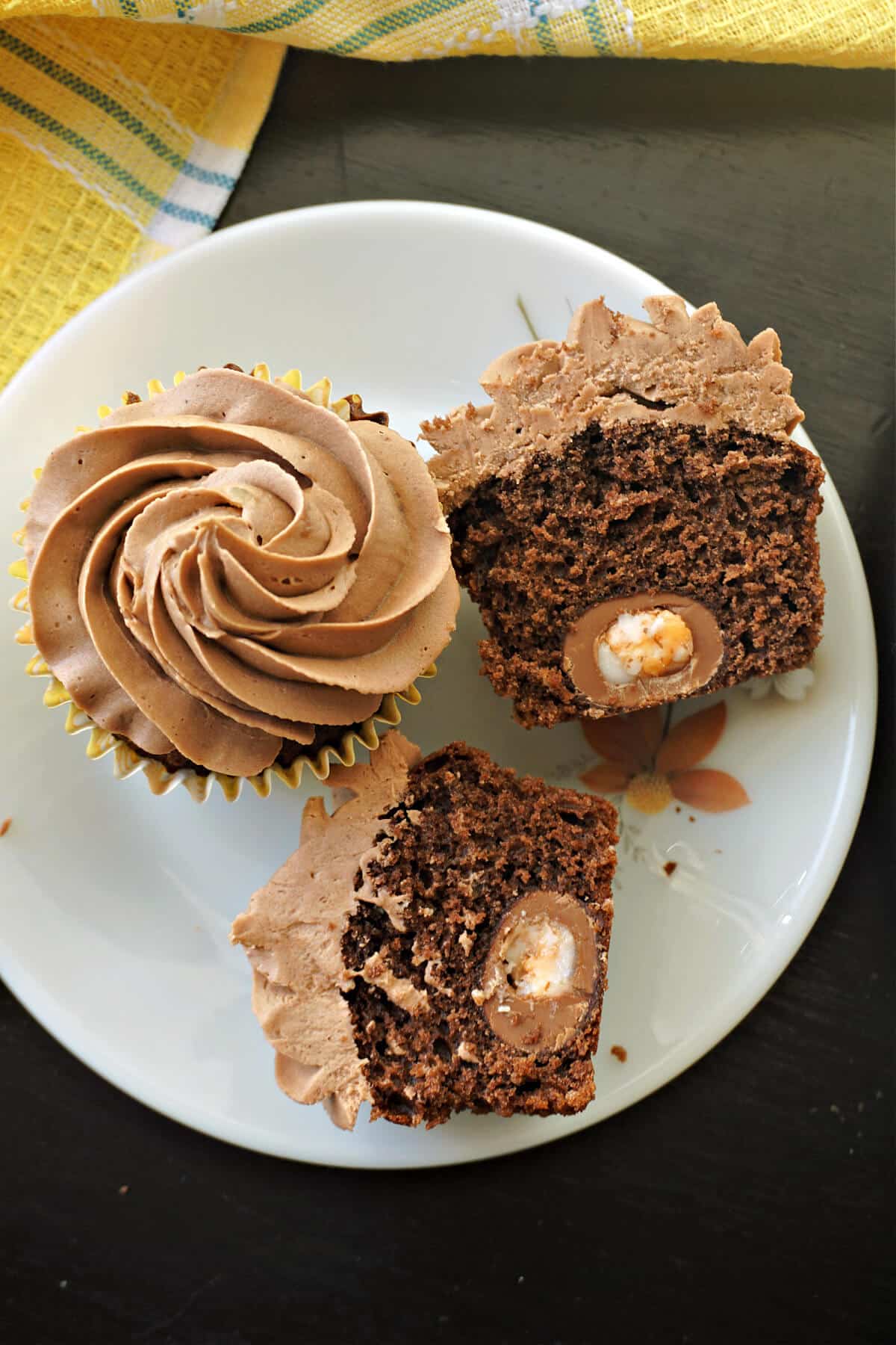 2 halves of creme egg cupcakes and a whole cupcake on a white plate.