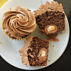 2 halves of a creme egg cupcake and a whole cupcake on a white plate.