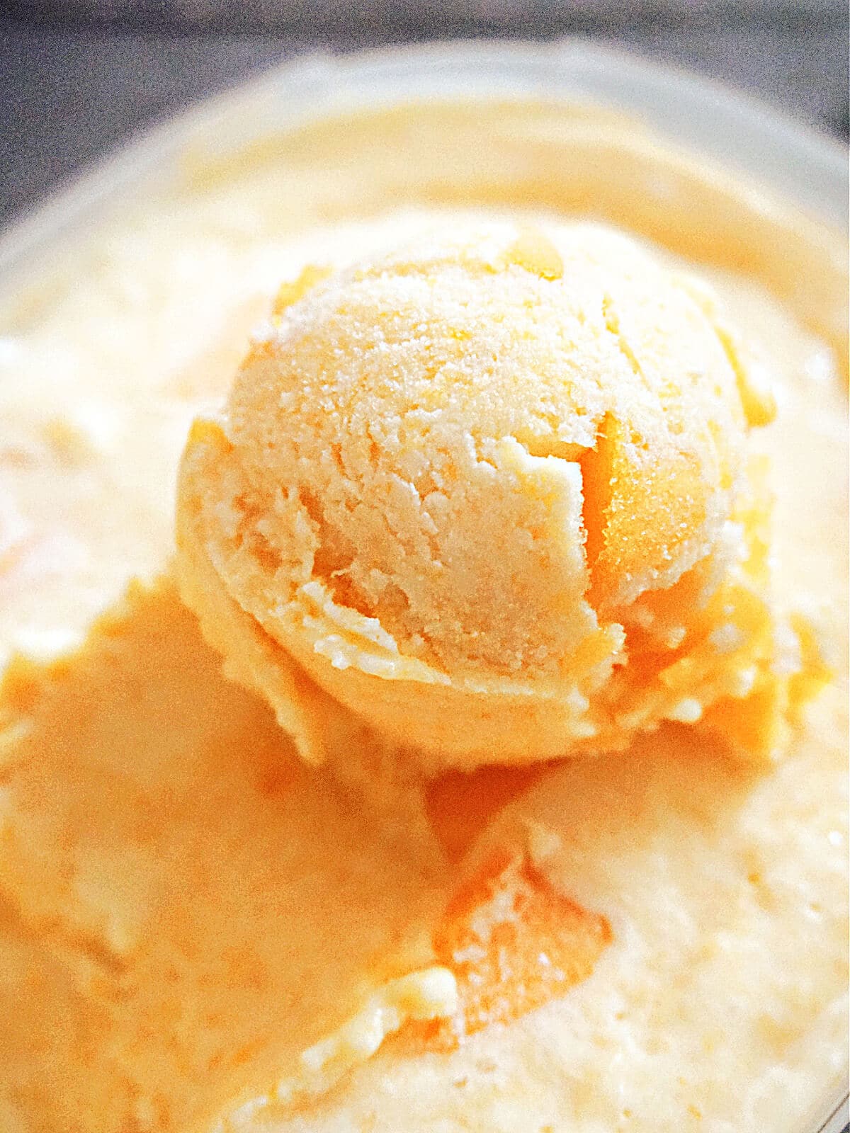 Close-up shot of a scoop of peach ice cream in an ice cream container .