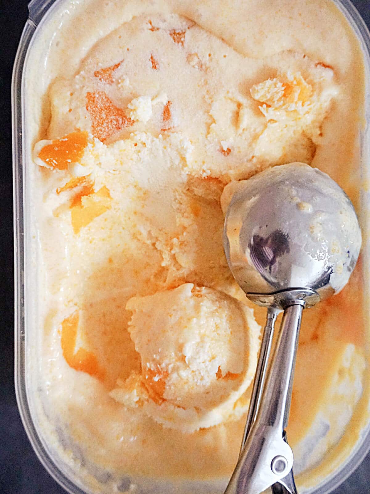 Overhead shot of a plastic container with peach ice cream and an ice cream scooper in it.