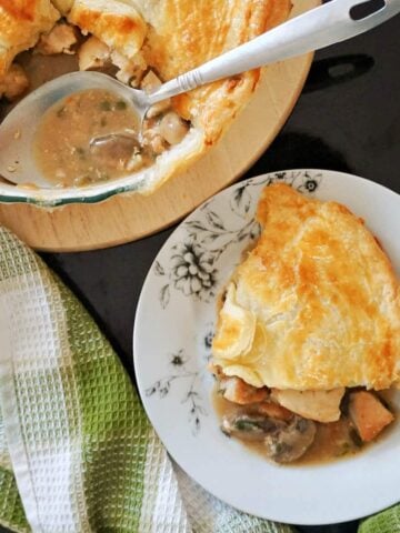 A white plate with a serving of chicken pie and a dish with more pie