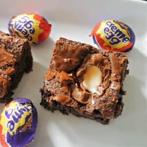 A slice of creme egg brownie with creme eggs around it.
