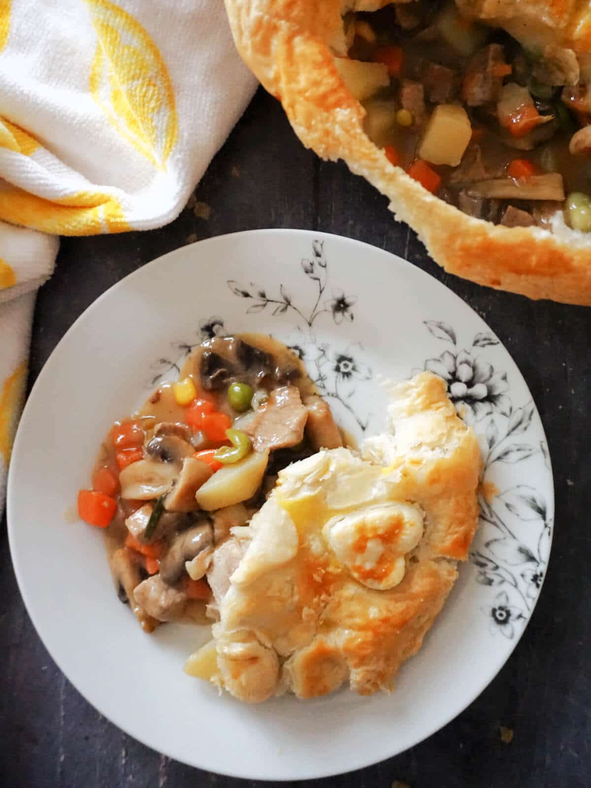 Overhead shot of a white plate with beef pie, a tea towel and a dish with more pie.