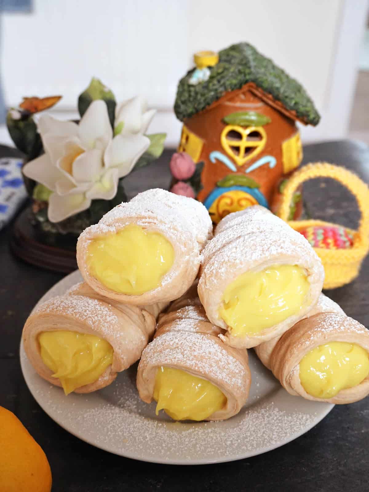 A pile of 5 cream horns on a white plate with decorations in the background.