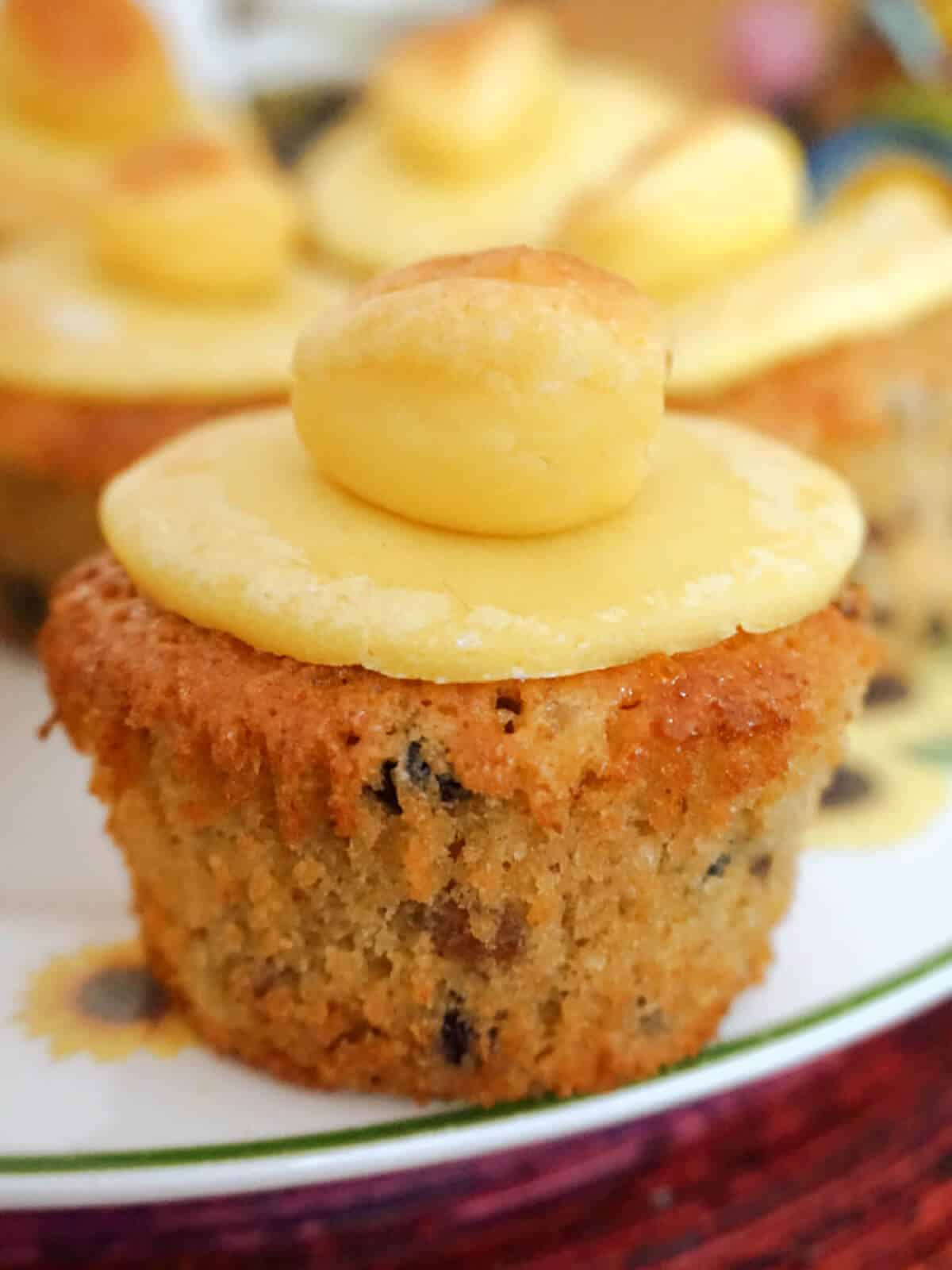 A simnel cupcake on a white plate with other muffins in the background.