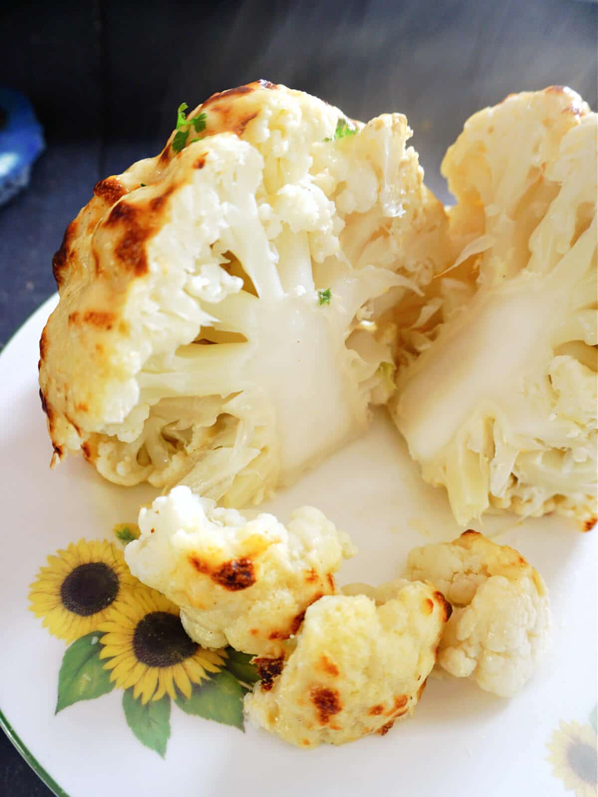 A whole roasted cauliflower cut into 2 halves and 2 florets on a white plate.