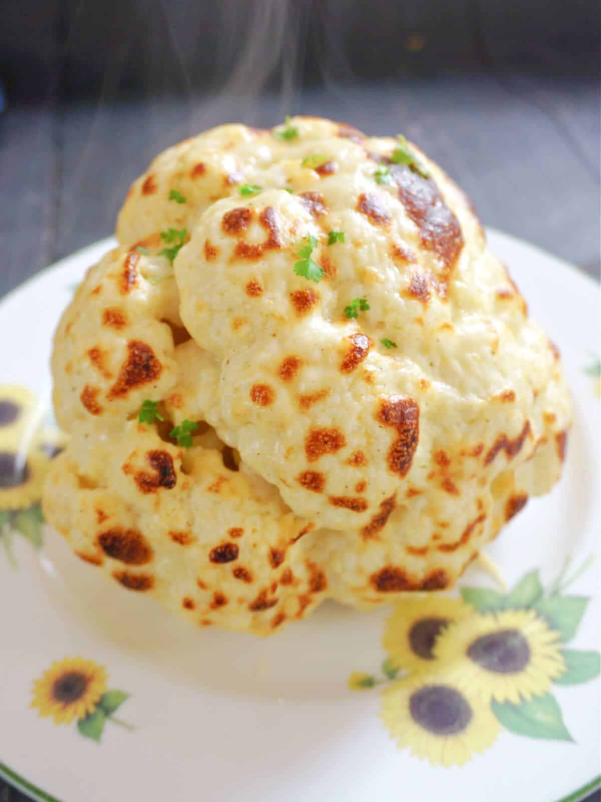 A whole roasted cauliflower on a white plate painted with sunflowers.