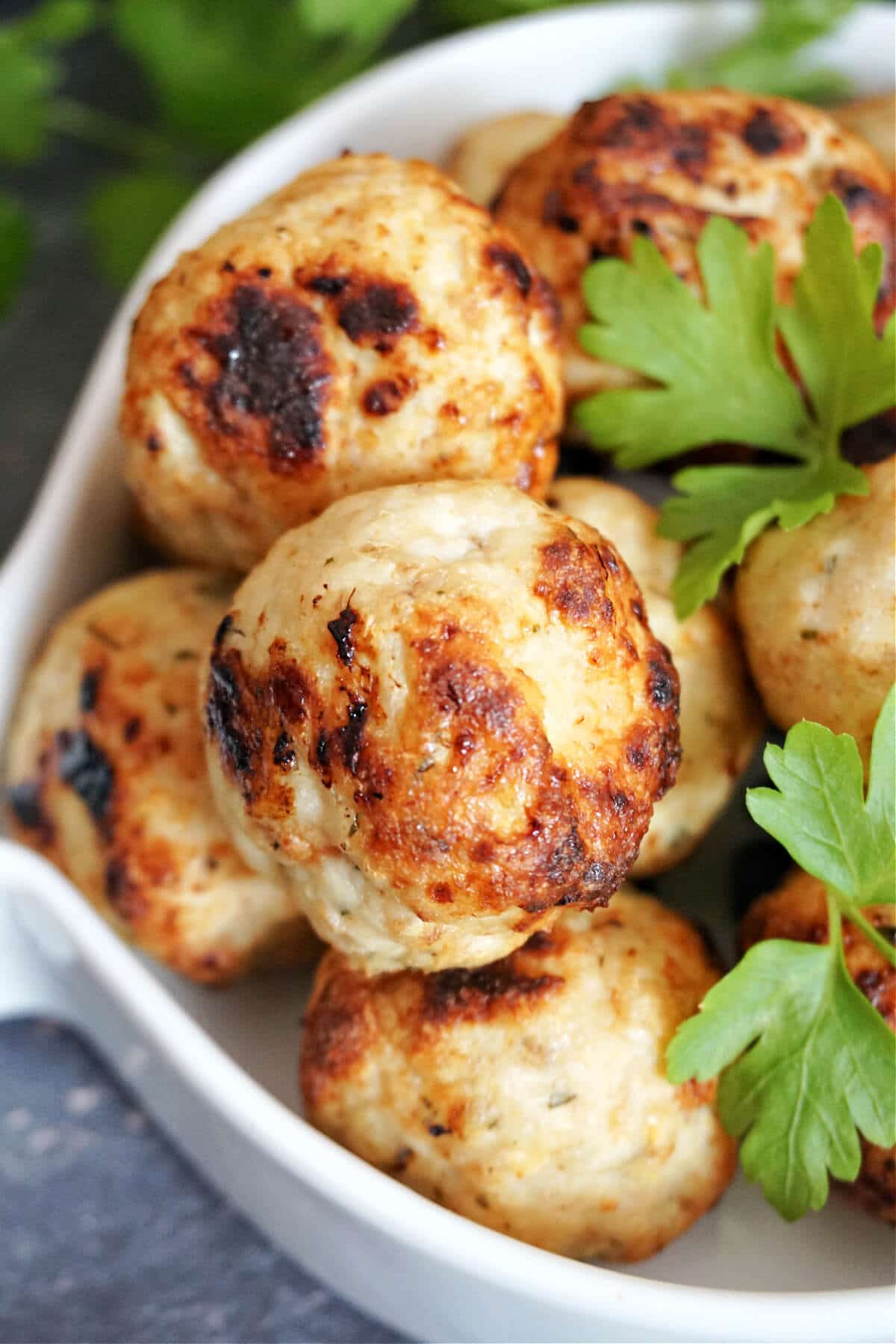 Chicken meatballs on a white serving bowl with fresh parsley leaves around.