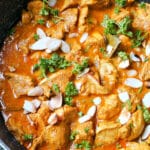 A pan with chicken korma garnished with parsley and almond flakes.