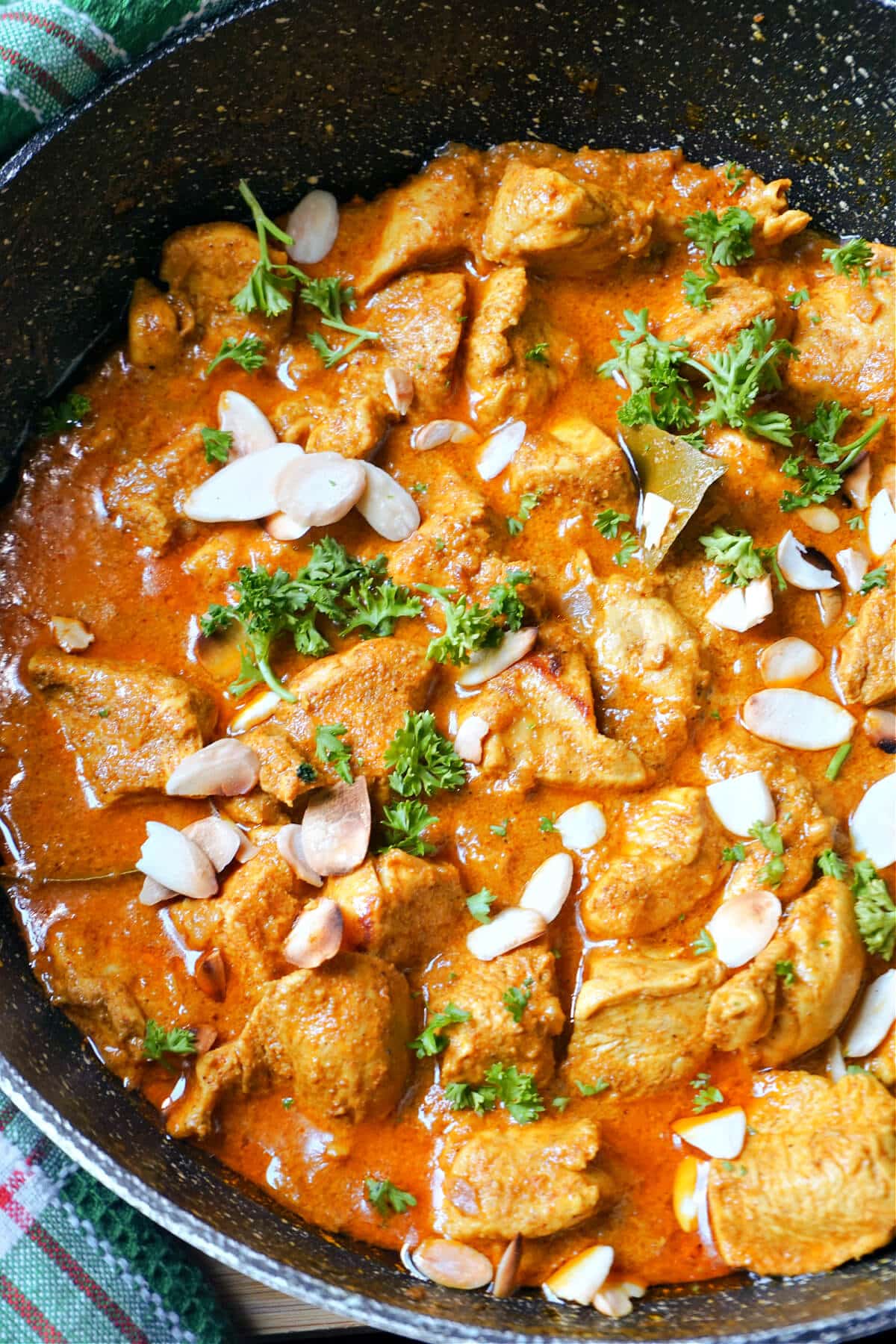 A pan with chicken curry garnished with parsley and almond flakes.