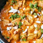 A pan with chicken korma garnished with fresh parsley and almond flakes.