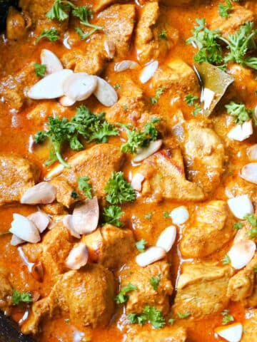 A pan with chicken korma garnished with fresh parsley and almond flakes.