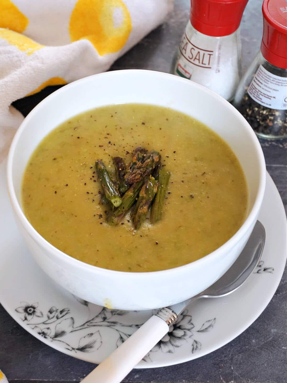 A white bowl of cream of asparagus soup topped with chopped roasted asparagus spears.