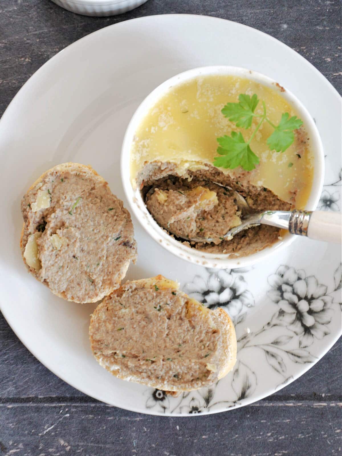 Overhead shot of a white ramekin with pate, 2 slices of baguette with more pate, everything arranged on a white plate.