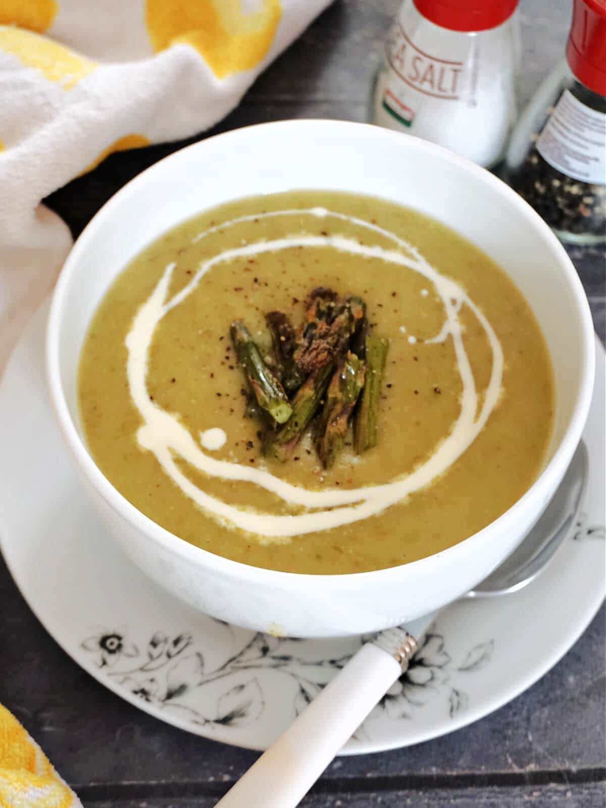A white bowl with roasted asparagus soup garnished with cream and asparagus spears
