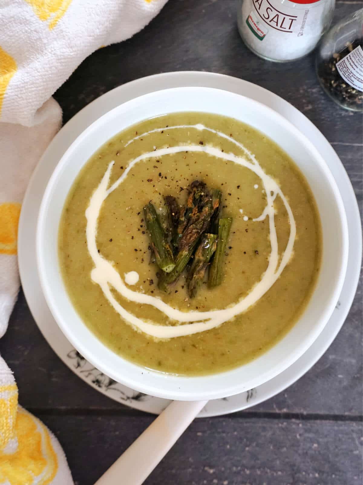 Overhead shot of a white bowl with creamy asparagus soup garnished with chopped asparagus and a drizzle of cream