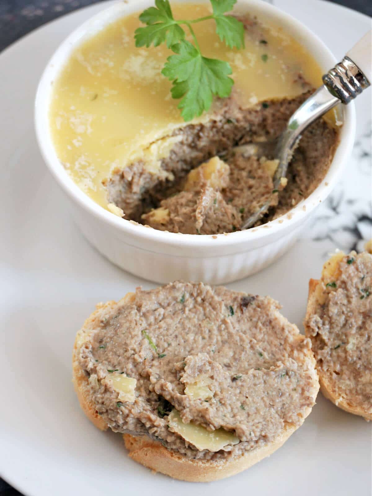 A white ramekin with mushroom pate and a slice of baguette spread with pate.