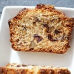 A slice of date and walnut cake on a white plate.