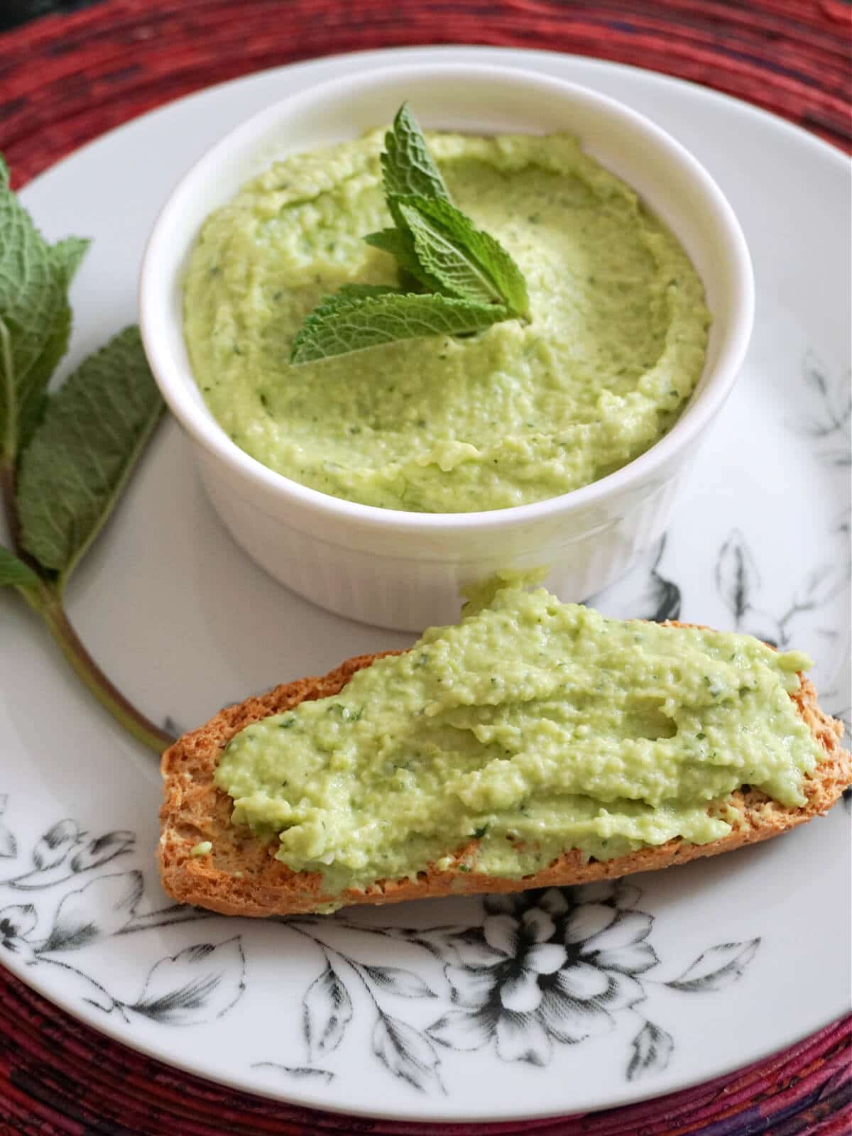 A white ramekin with broad bean dip and a toast spread with dip.