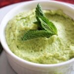 Close-up shot of a white ramekin with broad bean dip garnished with fresh mint leaves