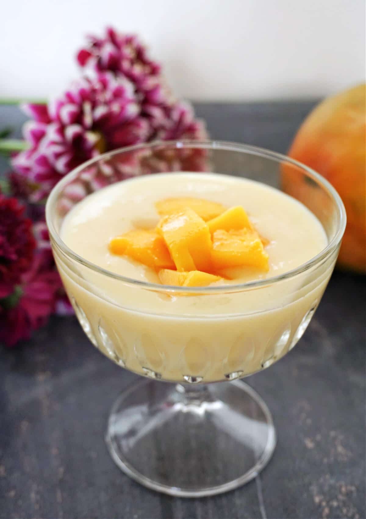 A glass with custard topped with mango chunks.