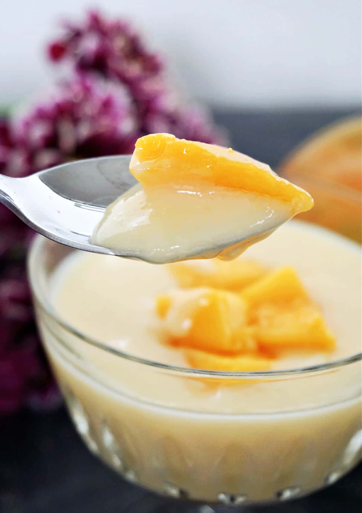 A spoonful of custard and mango piece over a glass with more custard and fruit