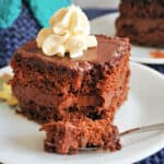 A white plate with a slice of chocolate cake and a fork cutting through the slice.