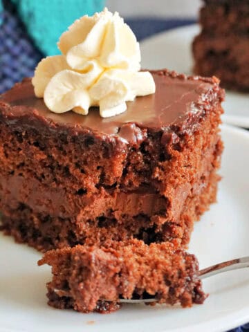 A white plate with a slice of chocolate cake and a fork cutting through the slice.