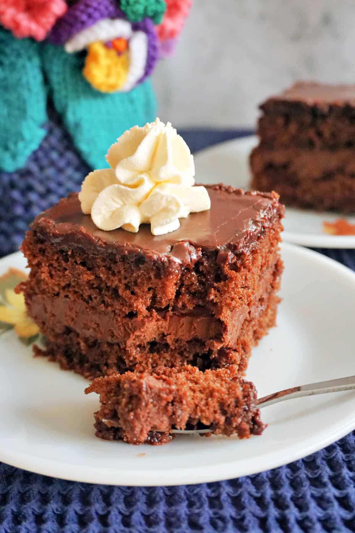 A white plate with a slice of chocolate cake topped with cream.