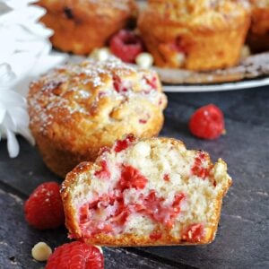 Half of a raspberry and white chocolate muffin with more muffins in the background