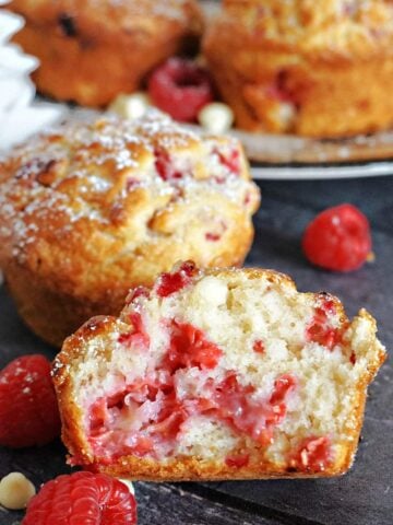 Half of a raspberry and white chocolate muffin with more muffins in the background