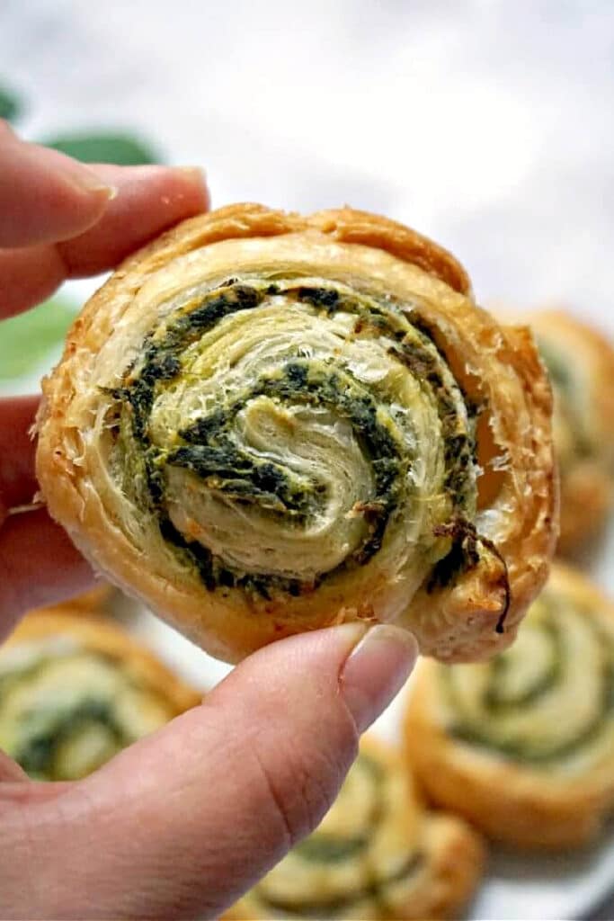 A hand holding a spinach pinwheel