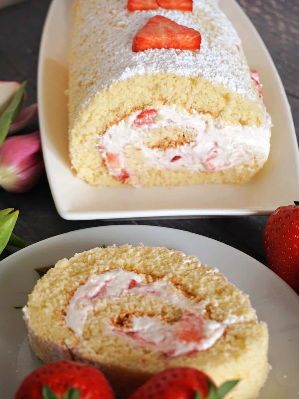 A cake roll on a rectangle plate with a round plate with a slice of cake roll