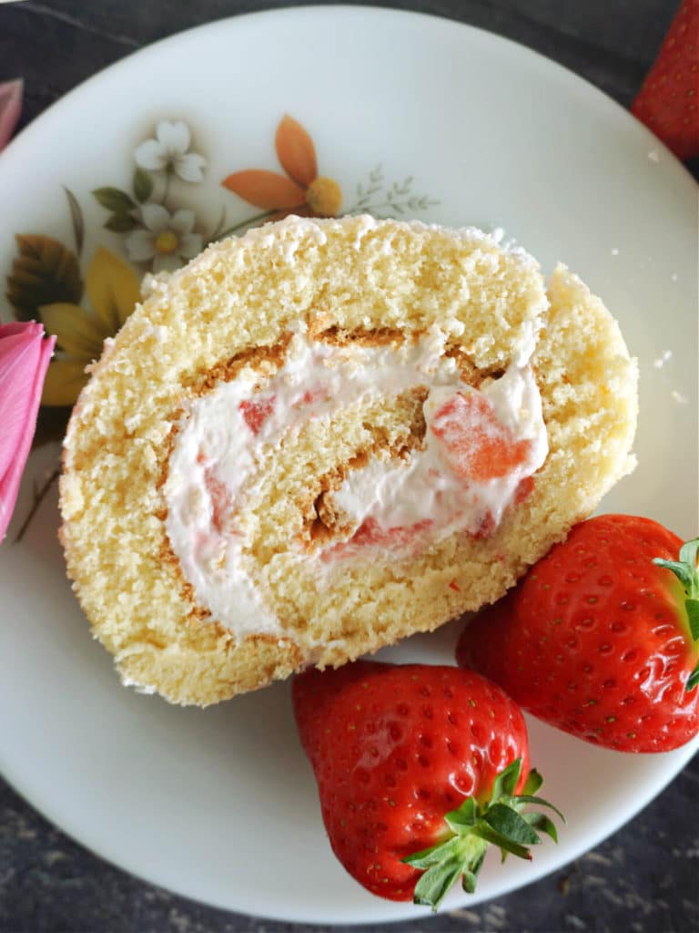 Overhead shot of a slice of strawberry cake roll on a white plate