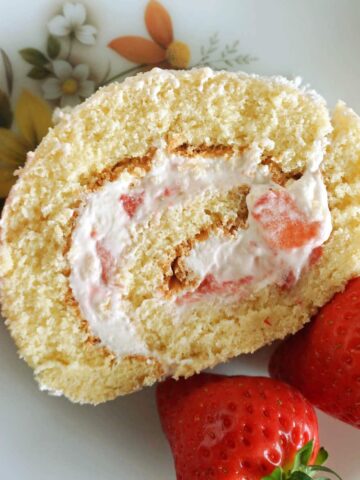 Overhead shot of a slice of strawberry cake roll on a white plate with 2 fresh strawberries on the side