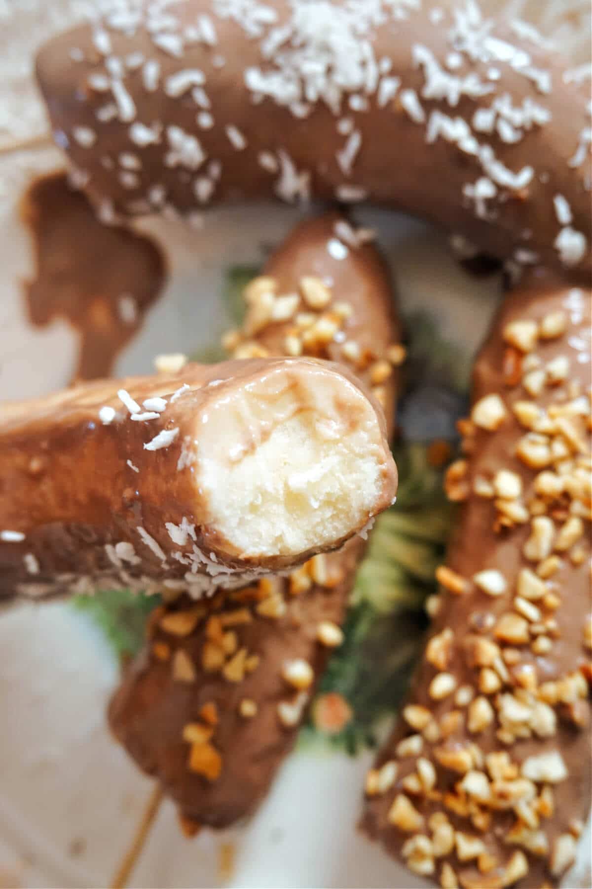A chocolate-covered banana bitten into it with more chocolate bananas in the background.