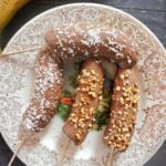 Overhead shot of 4 banana halves covered in chocolate and desiccated coconut and chopped nuts