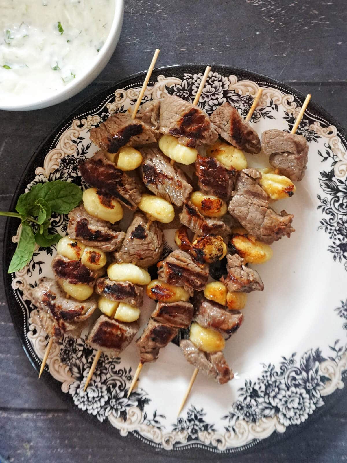 A plate with 4 skewers with gnocchi and beef cubes.